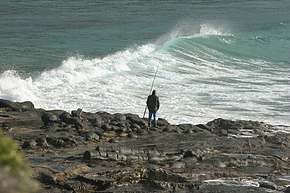Man waits by his fishing pole, watching the waves crest
