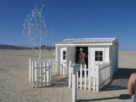 A small home with picket fence out in the deep desert, complete with mailbox full of gifts.