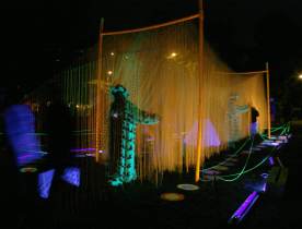 Array of plastic strings under black light at night, with blacklight cloaked participant