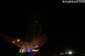 Above the Lepidodgera butterfly car, skydivers are trailing fireworks as they spiral down.