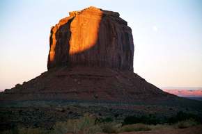 The moon rises over the butte at sunset