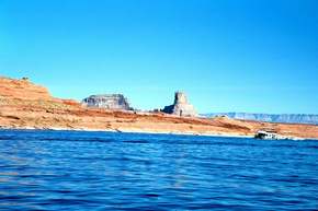 A houseboat steams by a butte on the side of Lake Powell